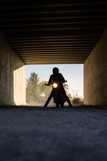 Silhouette of unrecognizable racer sitting on motorbike with switched on headlamps in tunnel