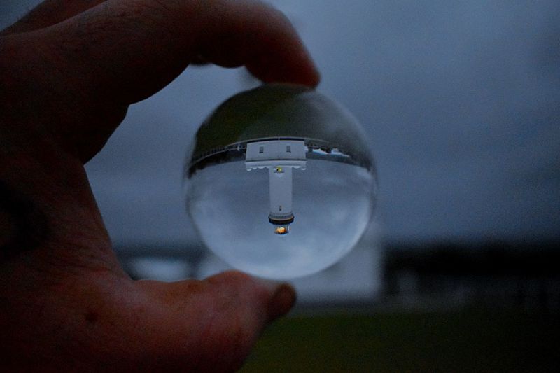Cropped hand holding crystal ball with reflection of lighthouse
