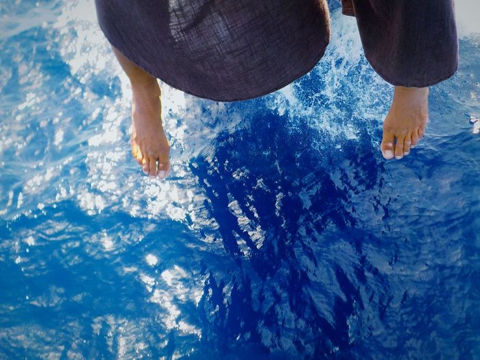 Low section of woman dangling feet over blue sea while sitting in ship