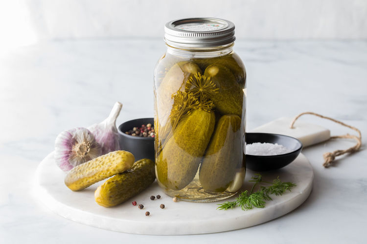 A jar of homemade pickles surrounded by ingredients, against a sunny window.