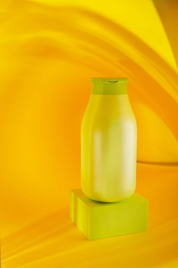 Close-up of yellow bottle on table against wall