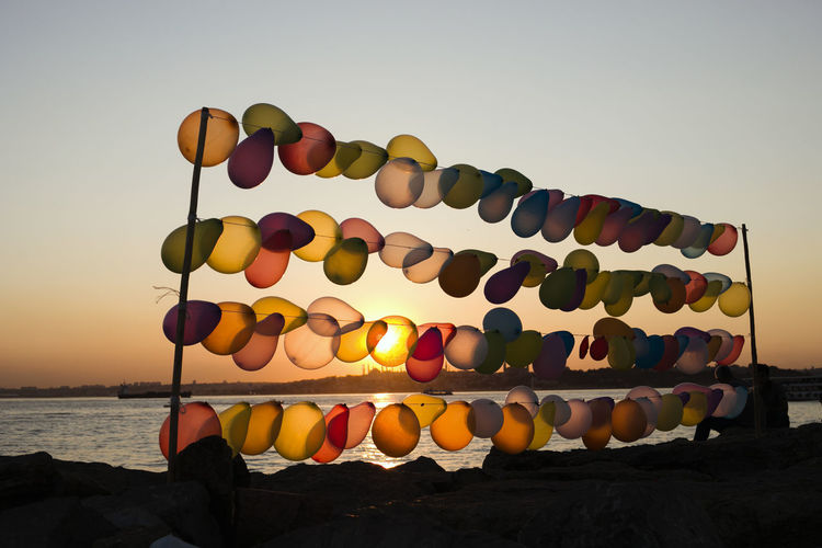 Multi colored balloons on rock by sea against clear sky