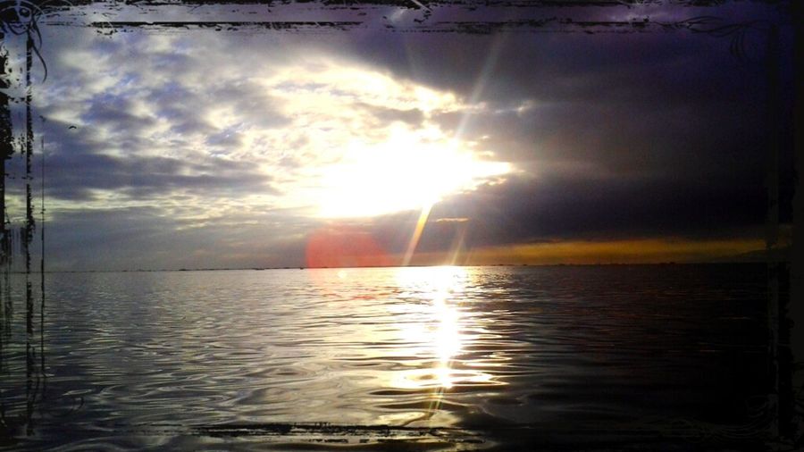 Sun shining through clouds over sea