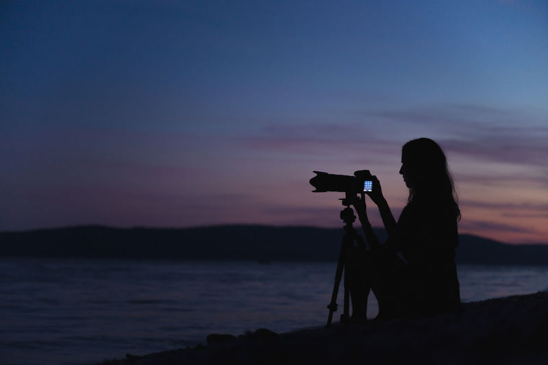 Silhouette person photographing against sky during sunset
