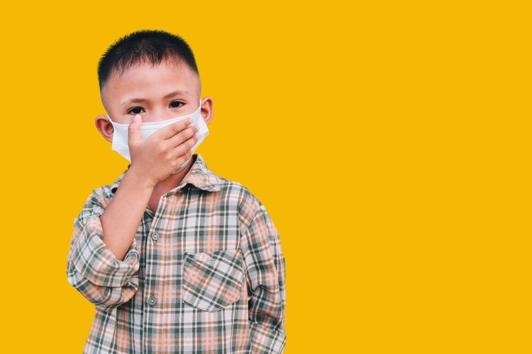 Portrait of boy standing against yellow background