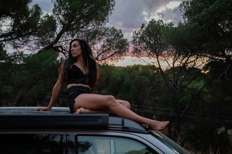 Full length of woman sitting on car against trees