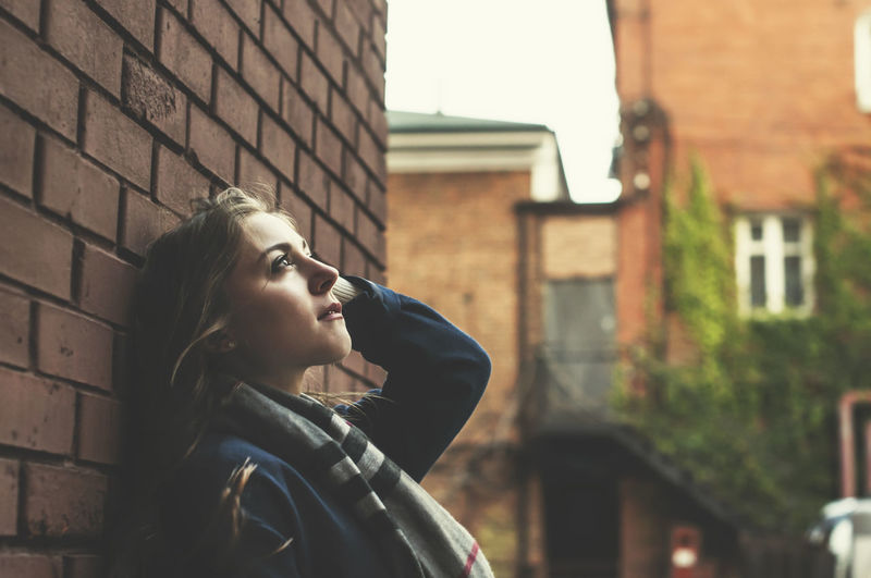 Portrait of young woman looking away against building