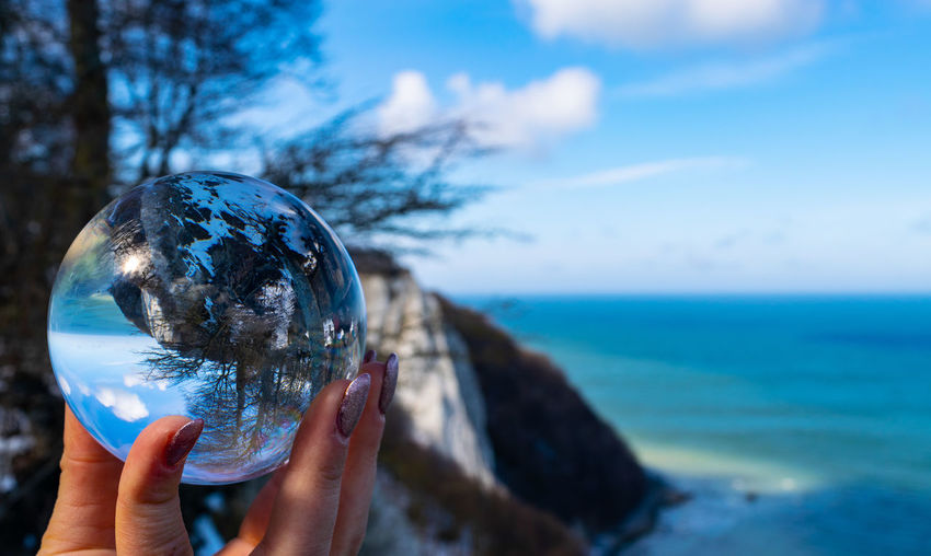 Cropped image of hand holding crystal ball against sea