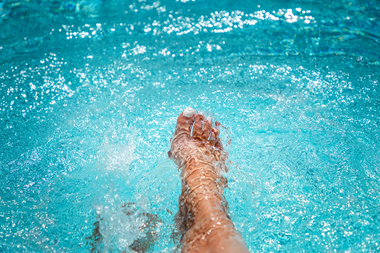 Feet from a caucasian woman splashing in the turquoise water of a pool person