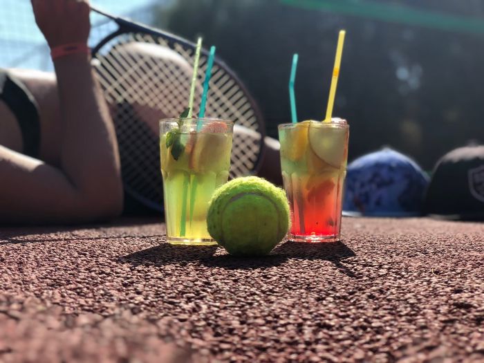 Close-up of tennis ball and drink in glasses at court