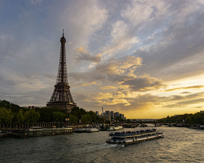 Eiffel tower by river against sky during sunset