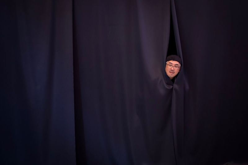 Close-up of a man looking through curtain