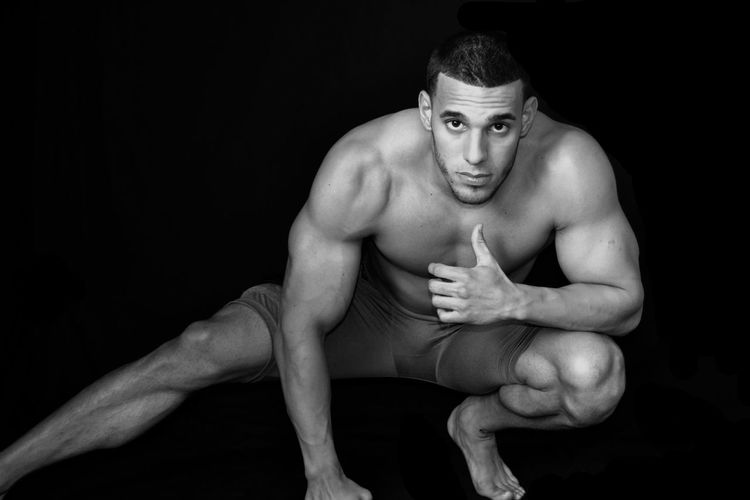 Portrait of young muscular man exercising against black background
