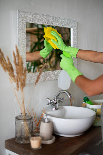 Cropped hand of woman cleaning mirror at home