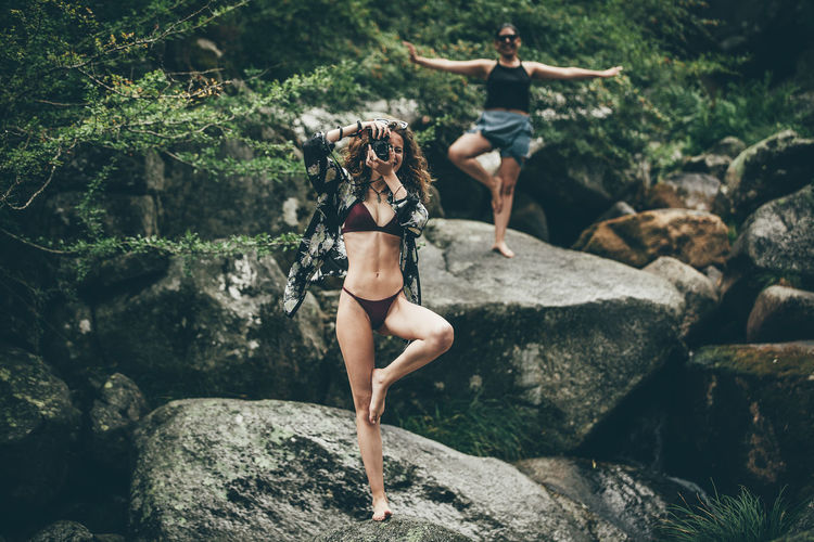 Woman photographing while doing yoga with friend in forest