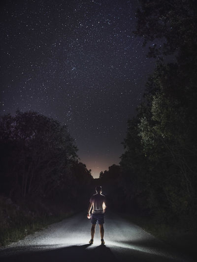 Rear view of man standing on road against sky at night