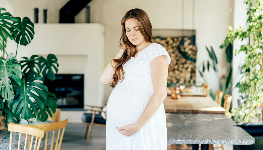 Long-haired pregnant woman in a white dress holds her belly. the concept of motherhood