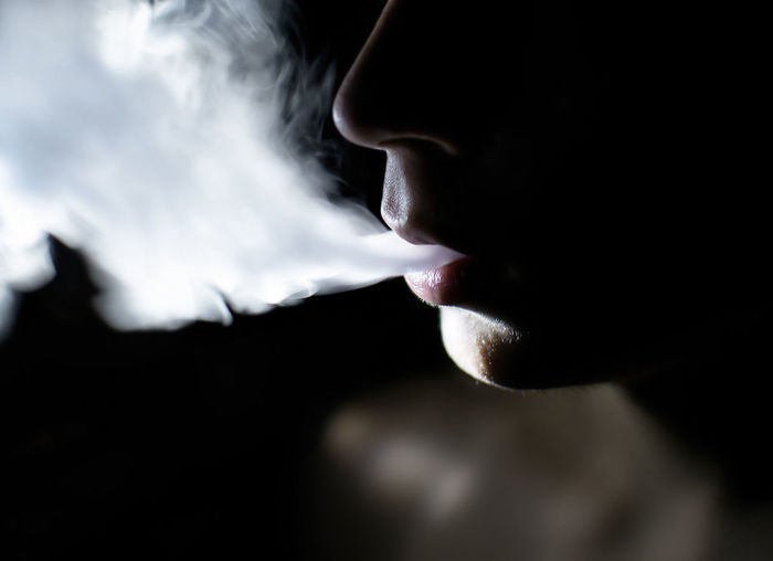 Cropped image of shirtless man smoking in dark