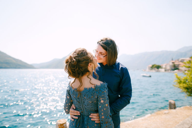 Bridegroom kissing while standing against lake