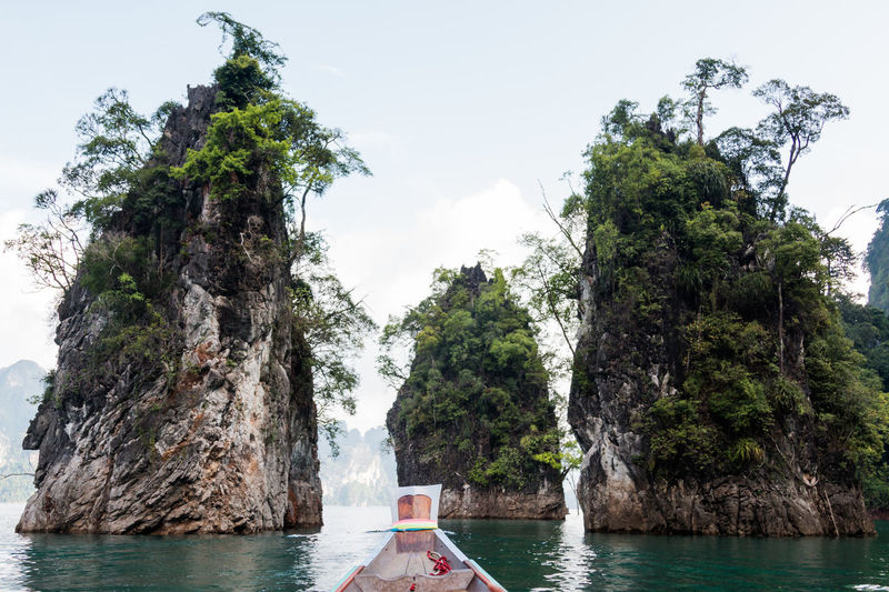 Rock formations in sea seen from long-tail boat against sky