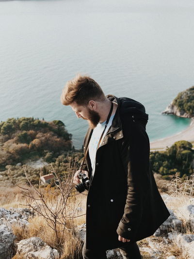 Side view of young man with camera standing on mountain