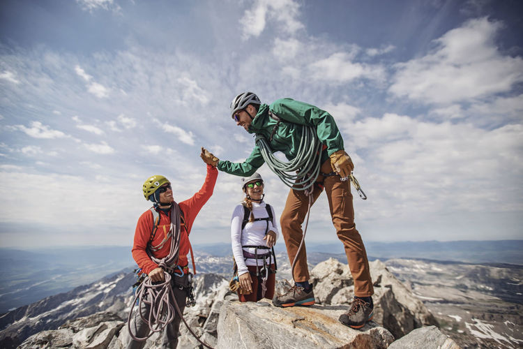 Two men high five at summit of grand teton while third person watches