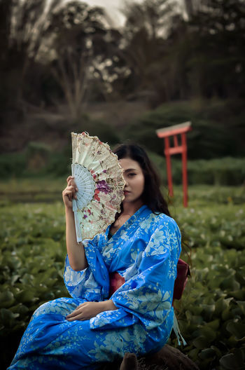 Young woman holding blue while sitting outdoors