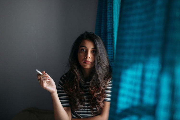 Portrait of woman smoking while sitting by window at home