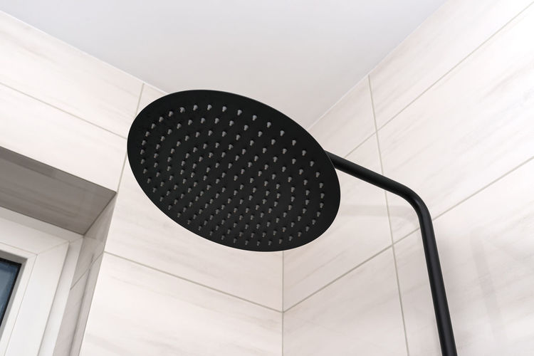 A modern, black metal shower with a large rain shower, placed on tiles.