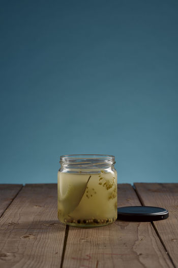 Jar with fond of gherkin pickles on wooden table with blue background