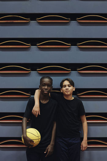 Portrait of teenage boy standing with arm around male friend at sports court