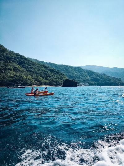 Distant view of male friends kayaking in sea against mountains