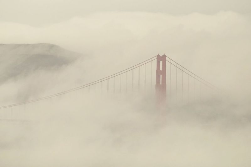 Suspension bridge in foggy weather against sky