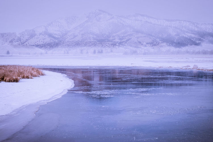 Scenic view of frozen lake by snowcapped mountains against sky