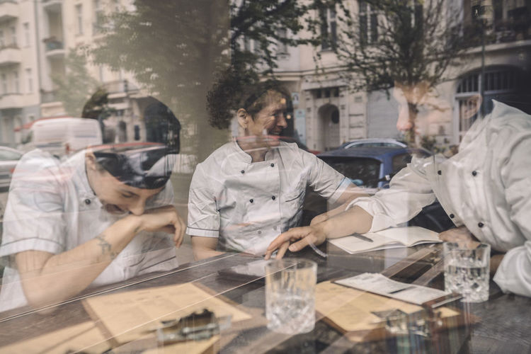 Happy coworkers sitting at restaurant table seen through glass window