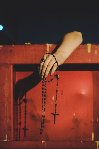Cropped hand holding rosary beads over surrounding wall at night