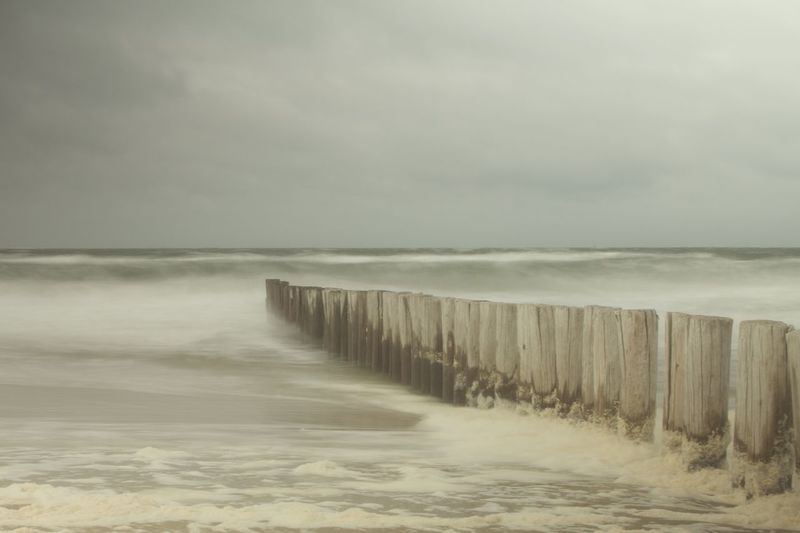 Wooden posts in sea against sky