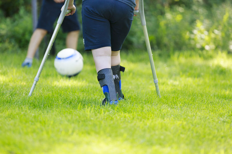 Low section of child using crutches playing football