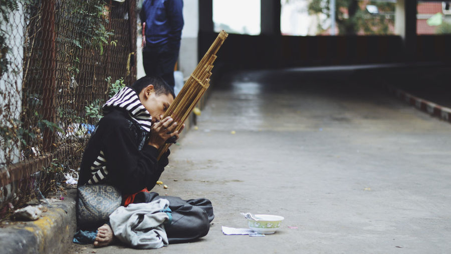 Beggar playing musical equipment while sitting on footpath