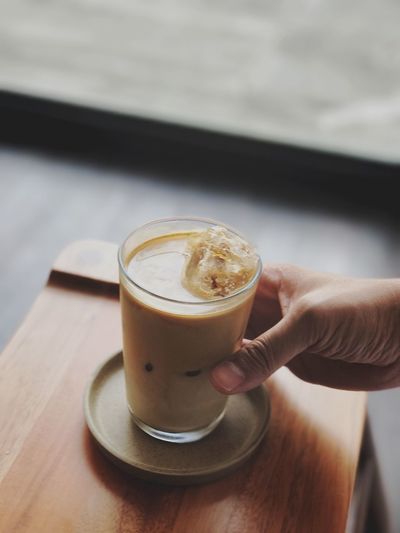Close-up of hand holding cappuccino served on table