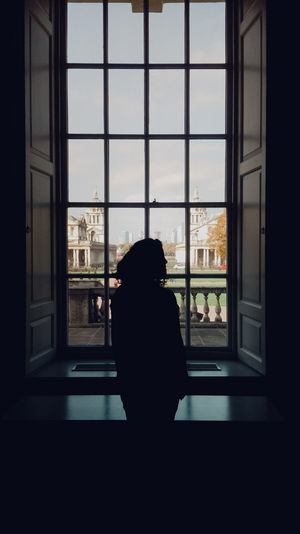 Silhouette woman looking through window