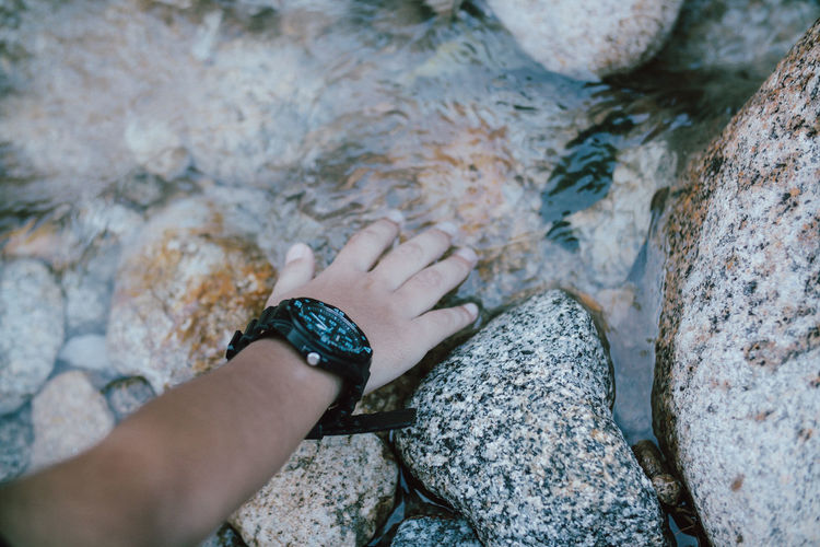 Cropped hand of person touching rock in stream