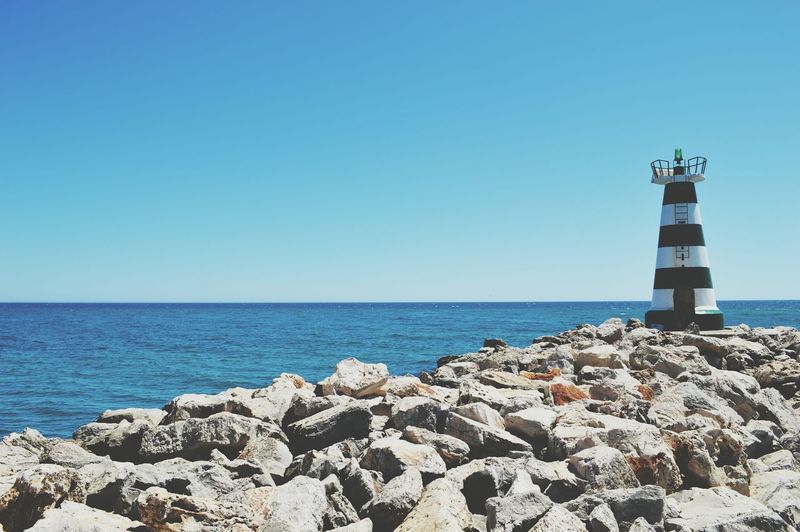 Lighthouse by blue sea against sky