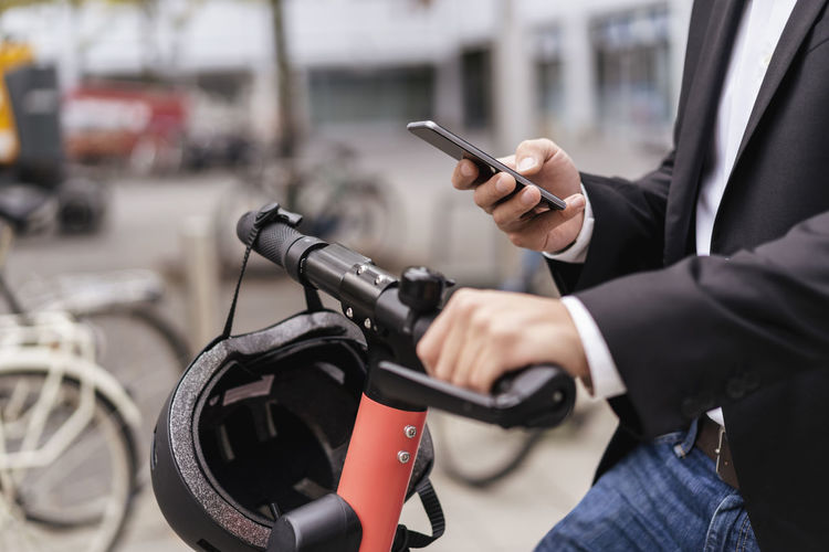 Close-up of businessman with e-scooter using cell phone in the city