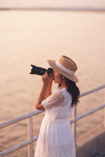 Woman wearing hat while standing by railing against sea