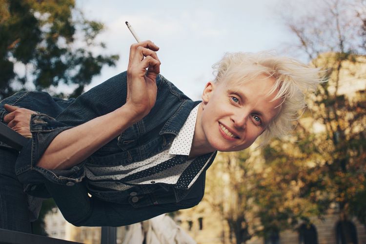 Mid adult woman holding cigarette while leaning on railing 