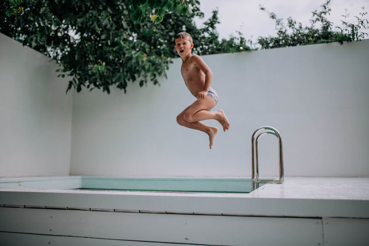 Full length of shirtless man jumping in swimming pool
