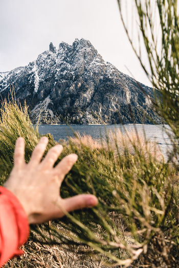 Cropped hand of person gesturing towards mountain against sky