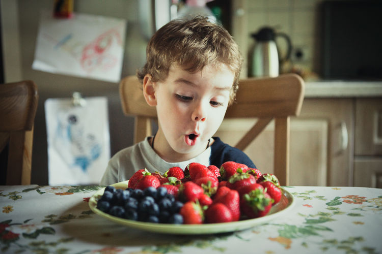 Cute boy looking at fruits in plate at table