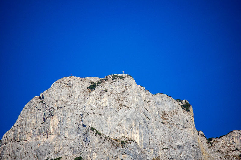 Low angle view of cliff on mountain against clear blue sky